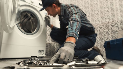 man is wasmachine aan het repareren